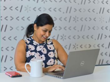 Image shows an associate working on a laptop with a cup of coffee next to it.
