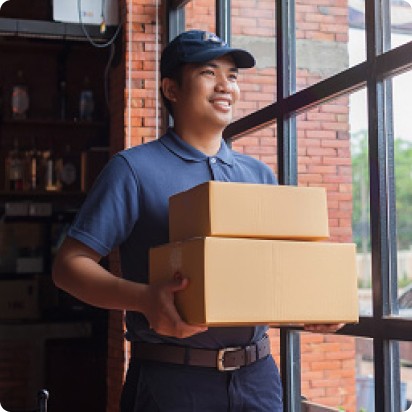 A smiling, male delivery person holding a stack of two medium-size packages.