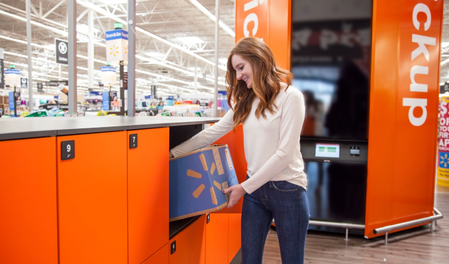 A smiling ginger haired female picking up a brown carton with Walmart logo from an orange locker