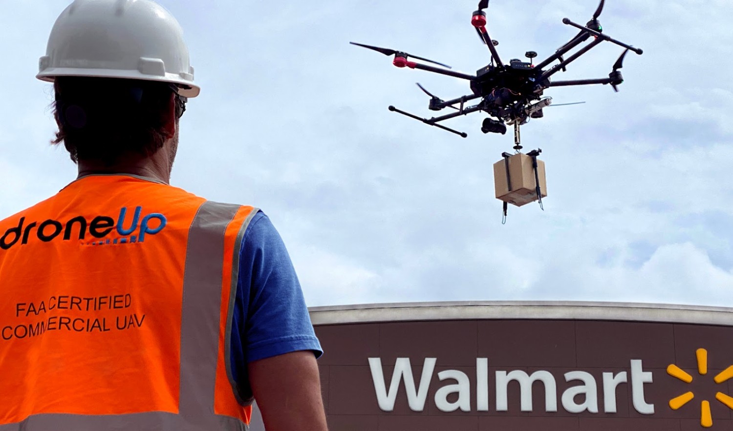 A drone in flight holding a carton for delivery over a Walmart storefront