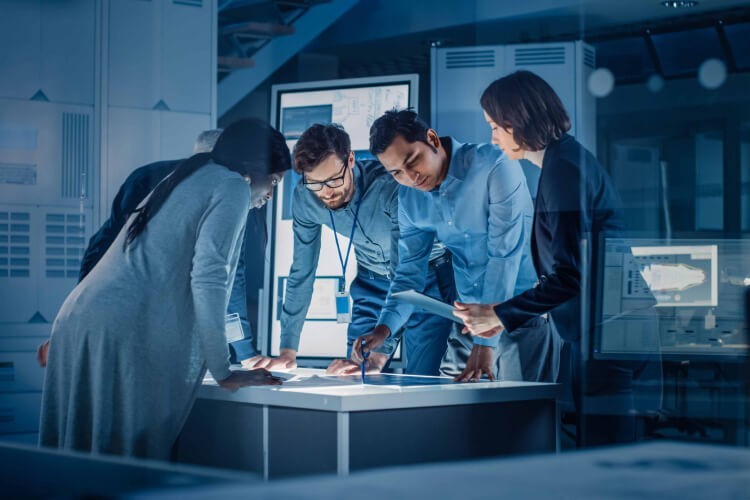 Four multiracial professionals seen in a huddle looking at documents on a table