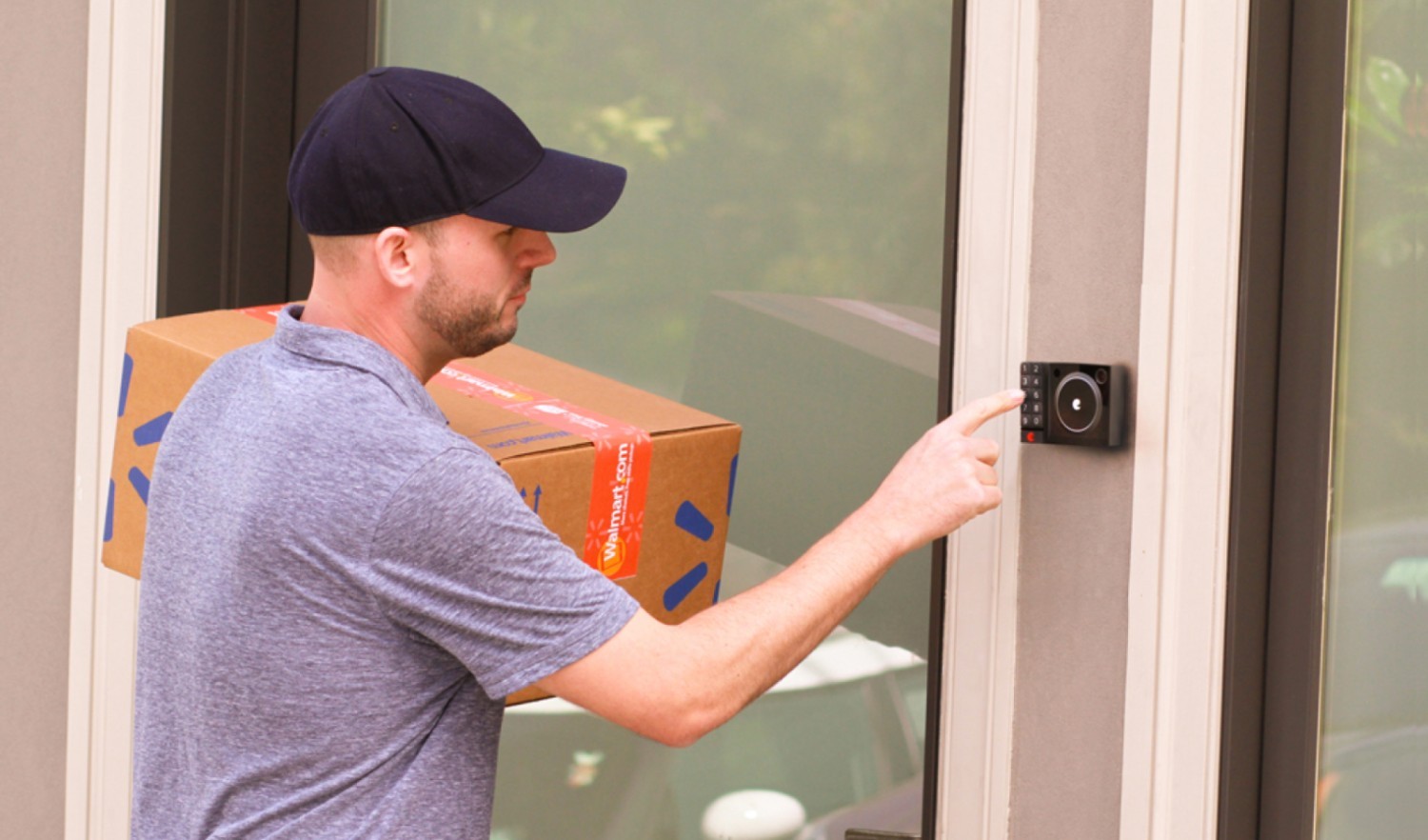 A capped delivery guy carrying on his shoulder a brown carton with Walmart logo